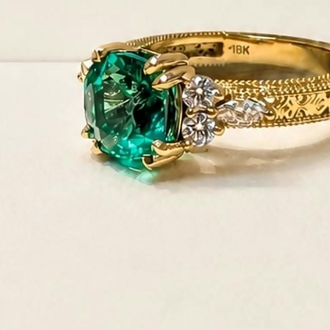 Anillo de oro de 18 quilates con una esmeralda talla cojín y hombros de diamantes, sobre fondo crema